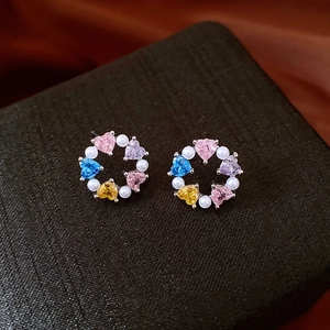 Macro shot of silver stud earrings with colorful heart zircon stones and small pearls