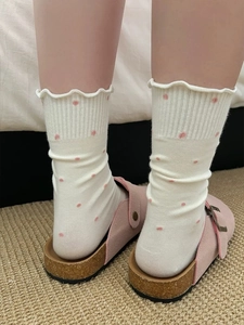 Close-up of white knit socks with pink polka dots and ruffled edges on pink slippers