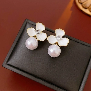 Detailed shot of gold floral earrings with square zircon and white pearl on black box