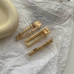 Detailed view of three acrylic hair clips with gold foil inlay on a white paper background