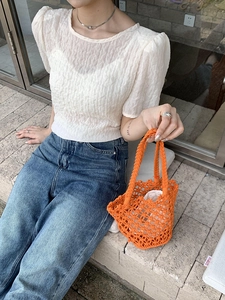 Orange handmade woven bucket bag with mesh detail held by model in outdoor setting