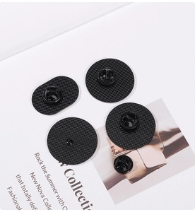 Detail of four black metal badge pin backs with textured grid surface and clutch fastener