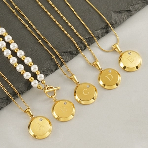 Classic 18K gold letter necklaces with small diamonds on grey stone slate background