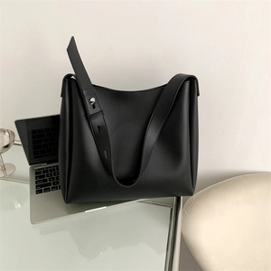 Detail of minimalist black tote bag with metal rivet buckle on glass desk workspace