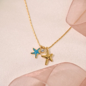 Charming gold star necklace with blue oil starfish and crystal on pink silk background