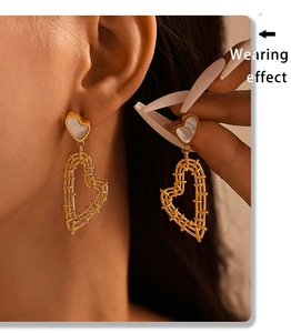 Close-up of heart-shaped gold woven earrings with white shell studs on female model