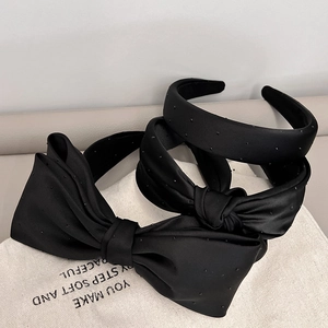 Elegant black satin headband with bow and polka dots on a neutral aesthetic background