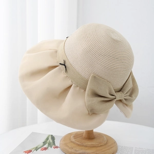 Detail of elegant beige sun hat with woven texture and large bow on a wooden stand