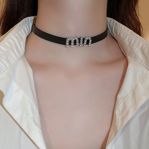 Macro detail of black leather choker featuring sparkly rhinestone miu letter charm