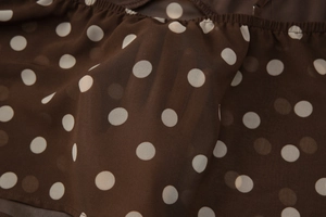 Gros plan sur tissu en mousseline marron à pois blancs montrant sa transparence