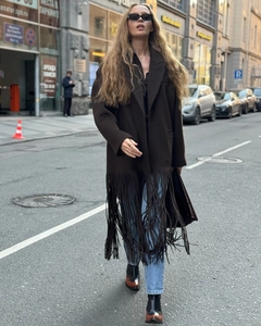 Street style view of a long dark brown woolen coat with thick fringe detail and wide lapels