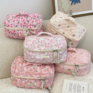 Stack of five quilted floral cosmetic bags in pink and beige on a plush white surface