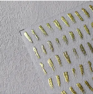 Macro shot of 3D metallic gold foil brushstroke nail stickers on lavender background