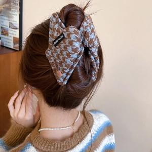 Detail showing handmade houndstooth bow hair clip with button on a textured knit fabric