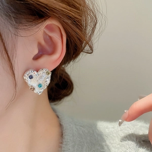 Close-up of heart-shaped silver earring with molten texture and colorful gemstones
