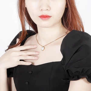 Detail of a golden heart pendant necklace with white inlay worn on a model