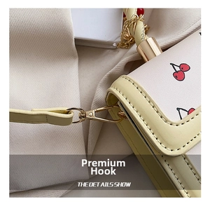 Detailed close-up of cherry pattern print and gold metal hooks on a cream yellow bag