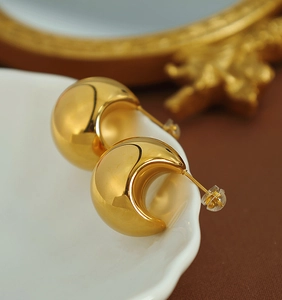 Macro shot of chunky gold crescent hoop earrings with high-polish finish on a tray