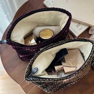 Macro view of woven tweed makeup bags with large zipper openings on a wooden table