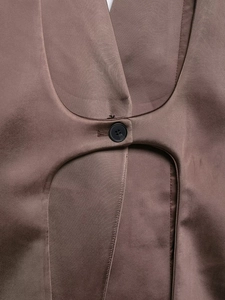 Detail of brown satin blazer with curved cut-out and black button fastening texture