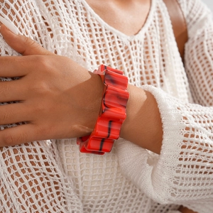 Macro detail of bold red acrylic wavy bracelet with black stripes worn by a model