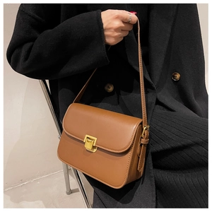 Close-up of brown vintage crossbody bag with gold square buckle worn with black coat