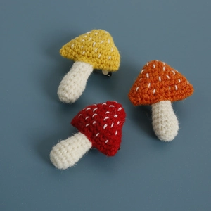 Three handmade crochet mushroom pins in red, yellow, and orange on a blue background