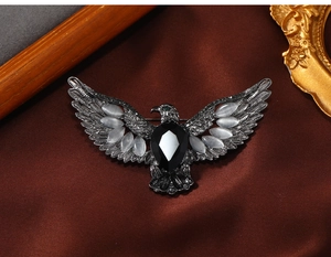 Detail of vintage eagle brooch with white cat eye stones and black gem on silk background
