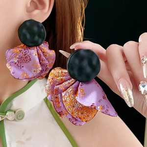 Detail of purple brocade flower earrings with black circular studs worn by a model