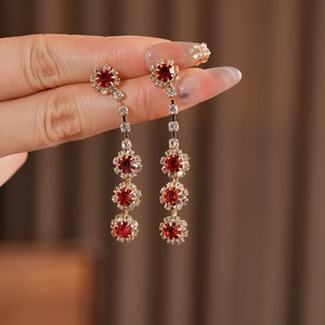 Close-up of long gold flower earrings with red gems and sparkling zirconia accents