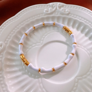 Dettaglio ravvicinato di un bracciale in smalto bianco a forma di bambù con anelli dorati