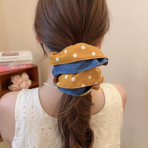 Close-up of a double-layered polka dot fabric scrunchie worn on a high ponytail style