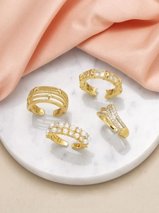 Detailed view of four 18k gold plated rings with pearls and zircons on marble coaster