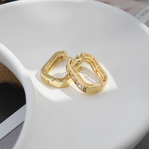 Macro shot of luxury gold geometric earrings with clear zircon stones on a white tray