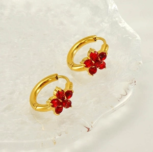 Vue macro de boucles d'oreilles créoles dorées avec détails de fleurs en zircon rouge