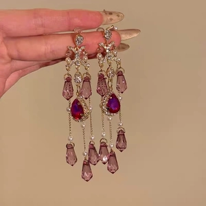 Macro shot of gold tassel earrings featuring purple teardrop crystals and small pearls