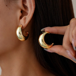Close-up of model wearing polished golden C-shape earrings with a smooth metallic finish