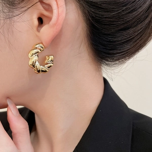 Close-up of golden twisted hoop earrings on model highlighting the metallic texture