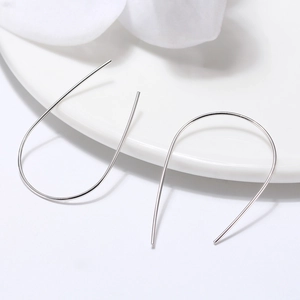 Close-up of minimalist S925 silver U-shaped curved earrings on a white ceramic tray
