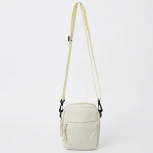 Minimalist cream canvas crossbody bag with adjustable black strap and front zipper pocket