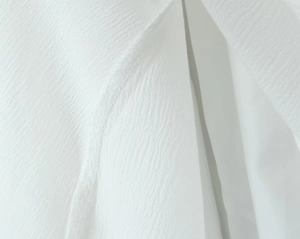Close-up of white dress fabric showing detailed texture, woven structure and quality stitching