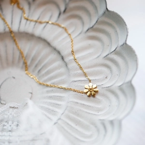 Elegant gold daisy pendant necklace on a vintage ceramic plate with lace detail