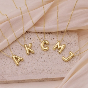 Close-up of golden balloon-style alphabet pendants on beige travertine with silk fabric