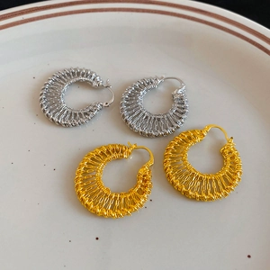 Macro shot of 18k gold and silver hollow woven C-shaped earrings on a ceramic dish