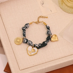 Detail of a handmade gold heart and rose pendant charm bracelet on a beige jewelry tray