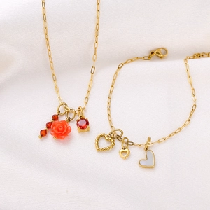 Detail of gold necklace and bracelet set with red floral and white heart pendants