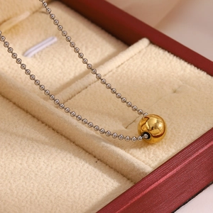 Close-up of minimalist stainless steel bead chain necklace with a golden ball pendant in a box