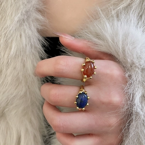 Detail view of two gold plated rings with oval orange and lapis blue stones on a model