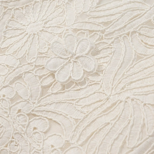 Detailed close-up of ivory floral embroidery and lace fabric on a skirt set