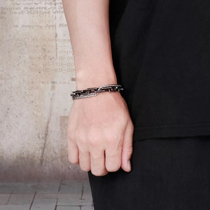 Detail of layered stainless steel Cuban chain bracelet on wrist with dark industrial style